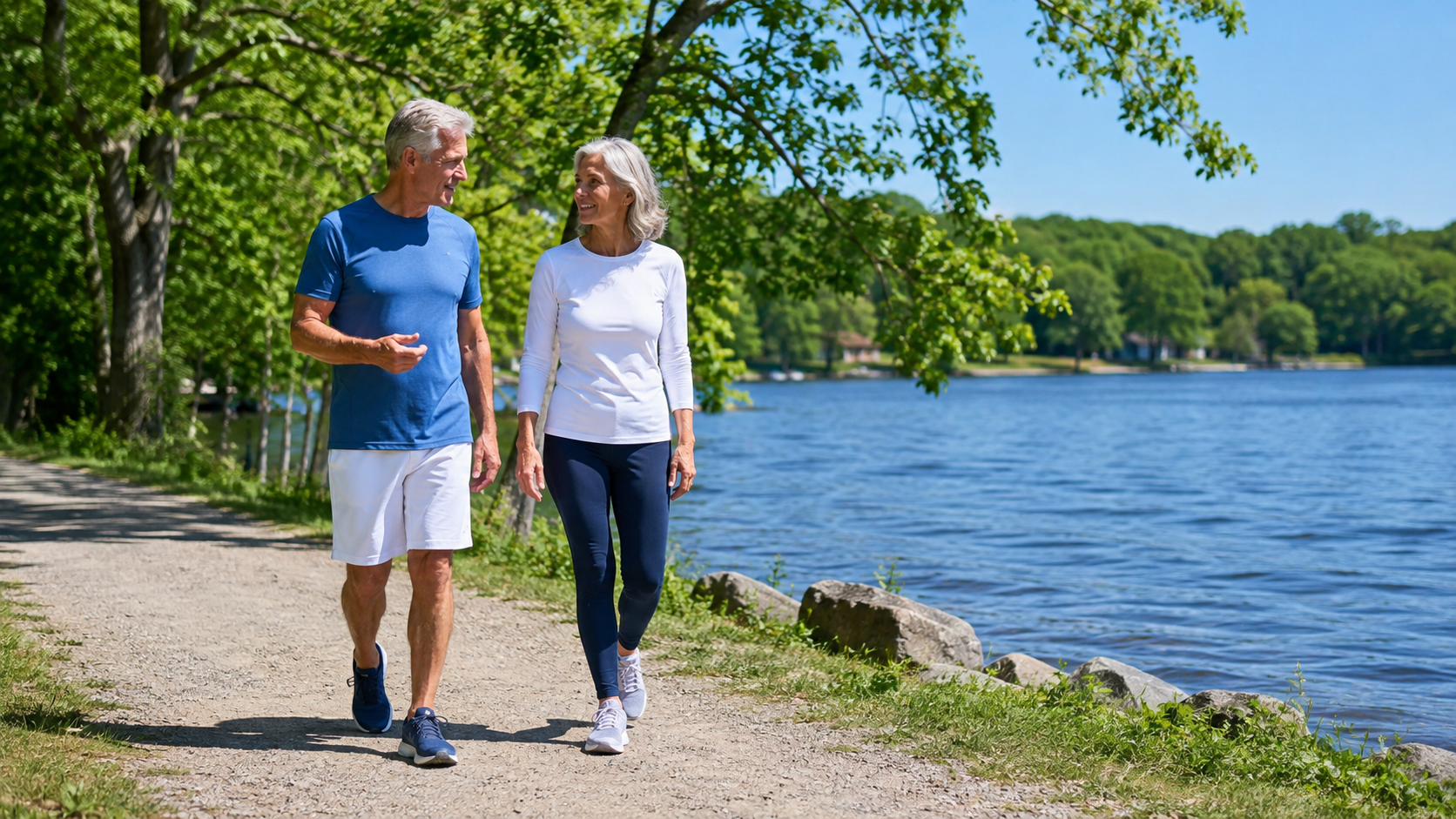 A man and woman in blue and white sportswear talking as they walk along a leafy path beside a blue lake.