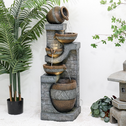 Decorative outdoor water fountain with stone and ceramic elements, surrounded by plants.